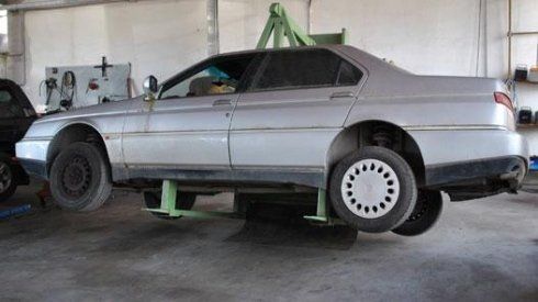 Un'auto argentata è parcheggiata su un sollevatore verde in un garage.