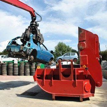 Un'auto blu viene sollevata da una gru in uno sfasciacarrozze.