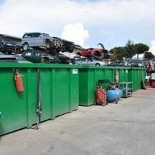 Una fila di cassonetti verdi pieni di automobili e attrezzi.
