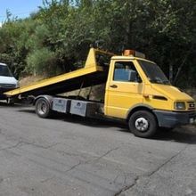 Un carro attrezzi giallo è parcheggiato sul ciglio della strada accanto a un furgone bianco.