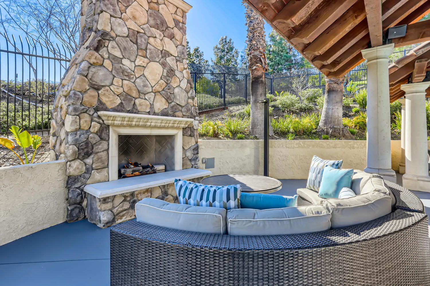 Outdoor stone fireplace with a circular wicker sectional sofa under a covered patio.
