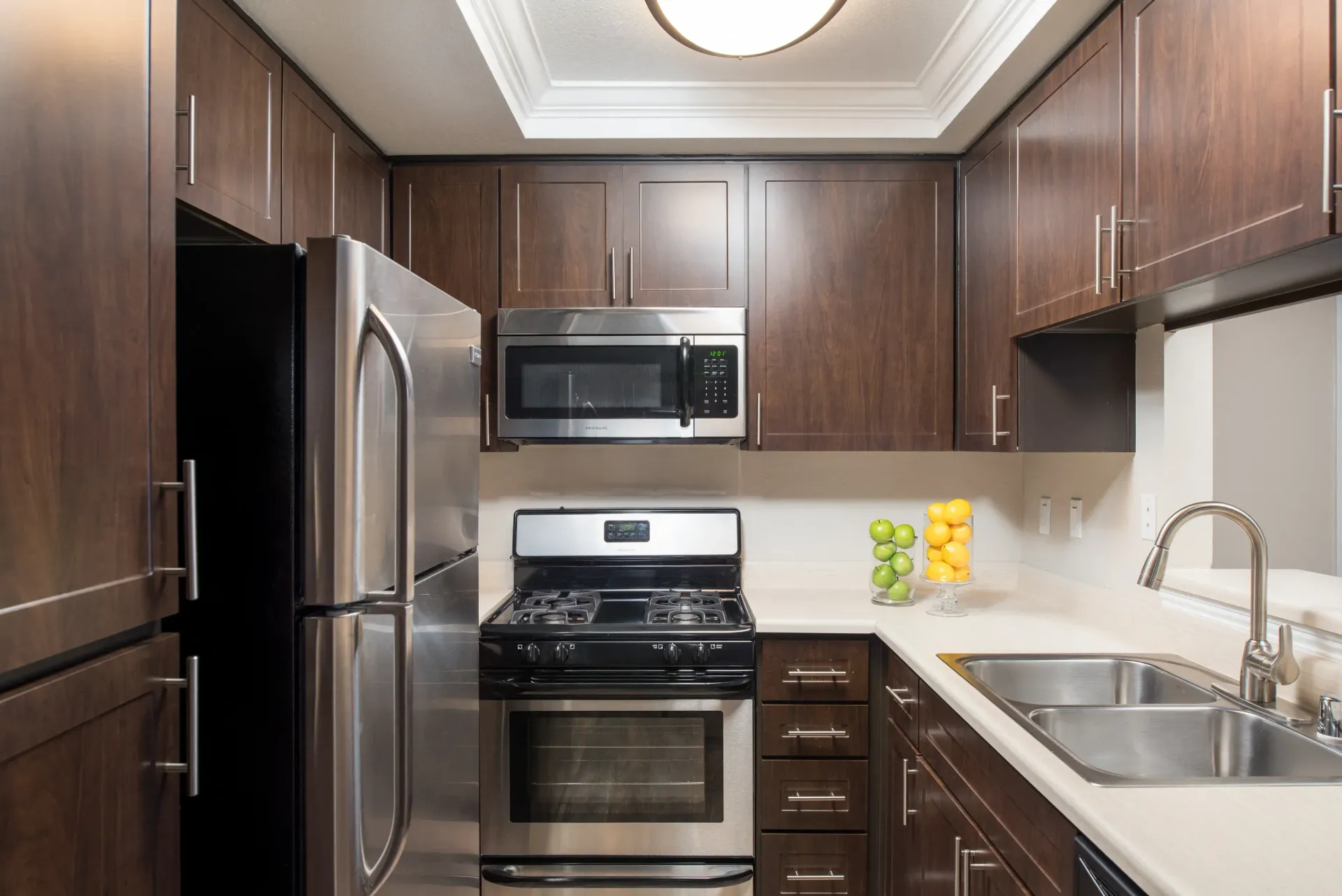 Modern kitchen with dark wood cabinets, stainless steel appliances, and a double sink.