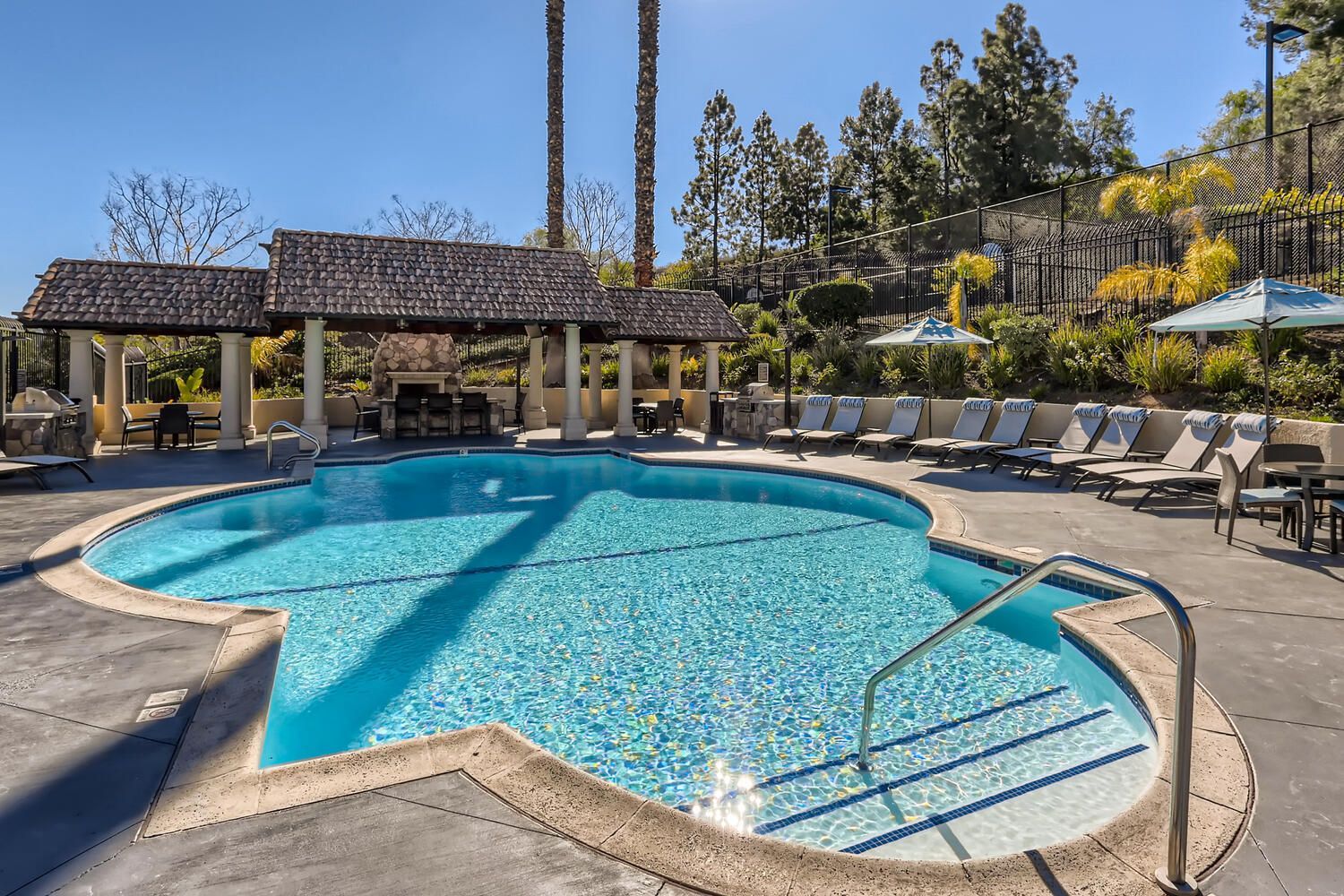 Outdoor community pool area with a shaded cabana, lounge chairs, and umbrellas.