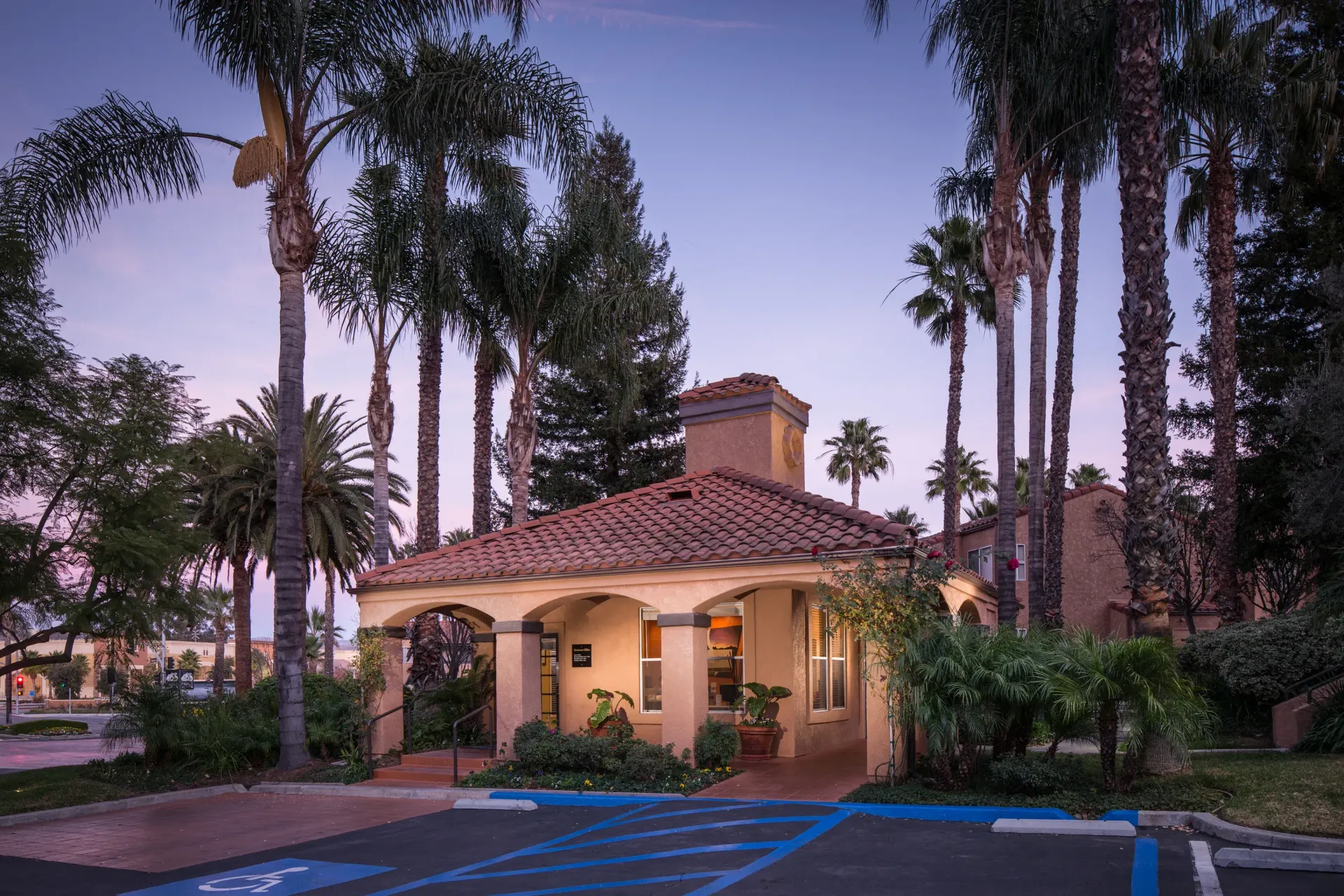 Exterior community clubhouse with arches, a red-tiled roof, and tall palm trees.