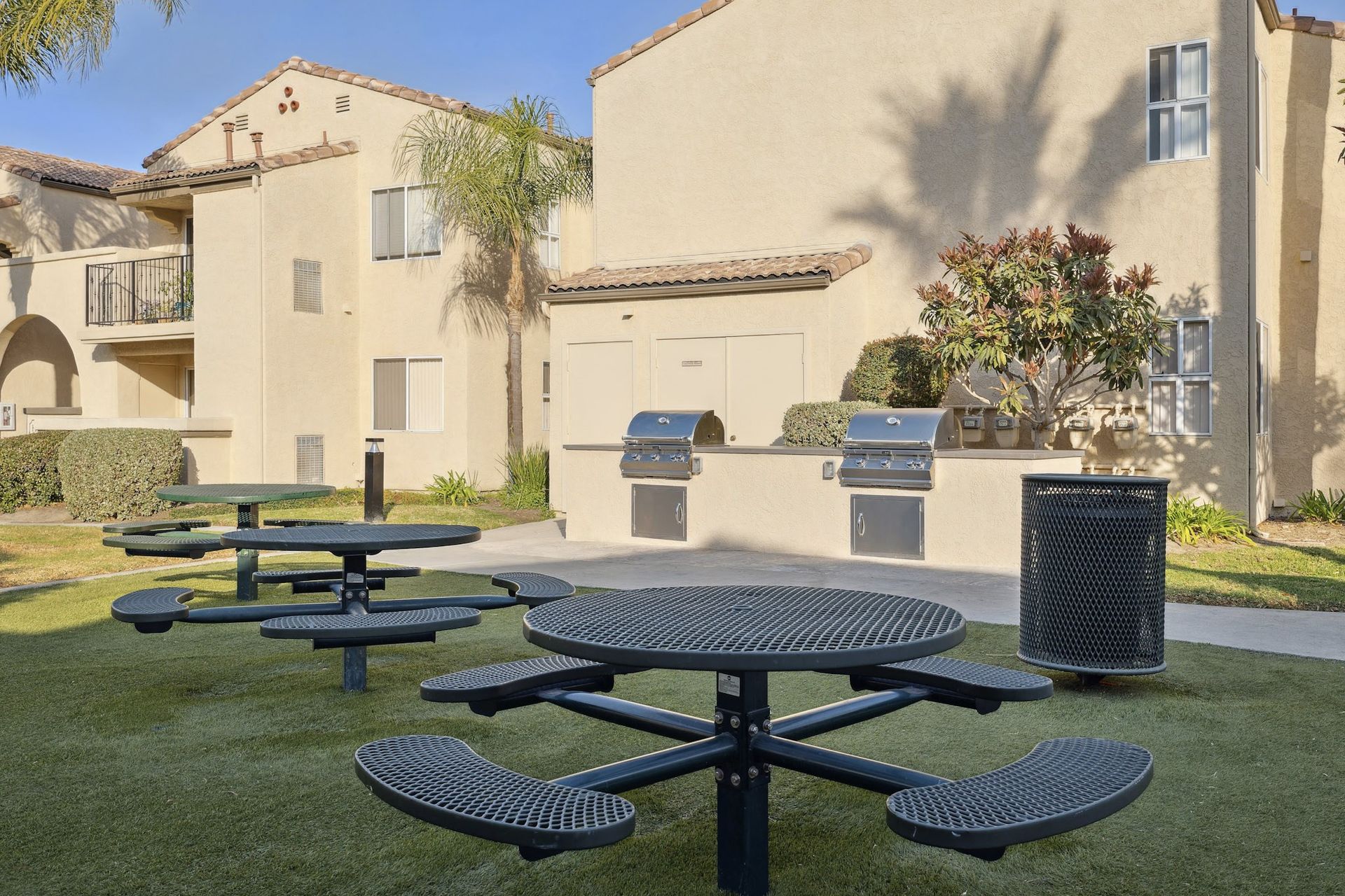 Exterior communal courtyard with round metal picnic tables, grills, and landscaping.