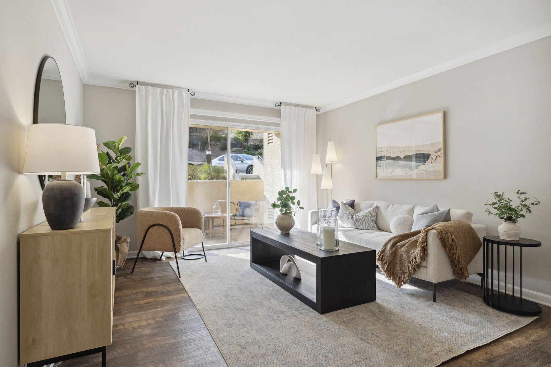 Living room in an apartment with sofa, coffee table, plants, and sliding glass door to balcony.