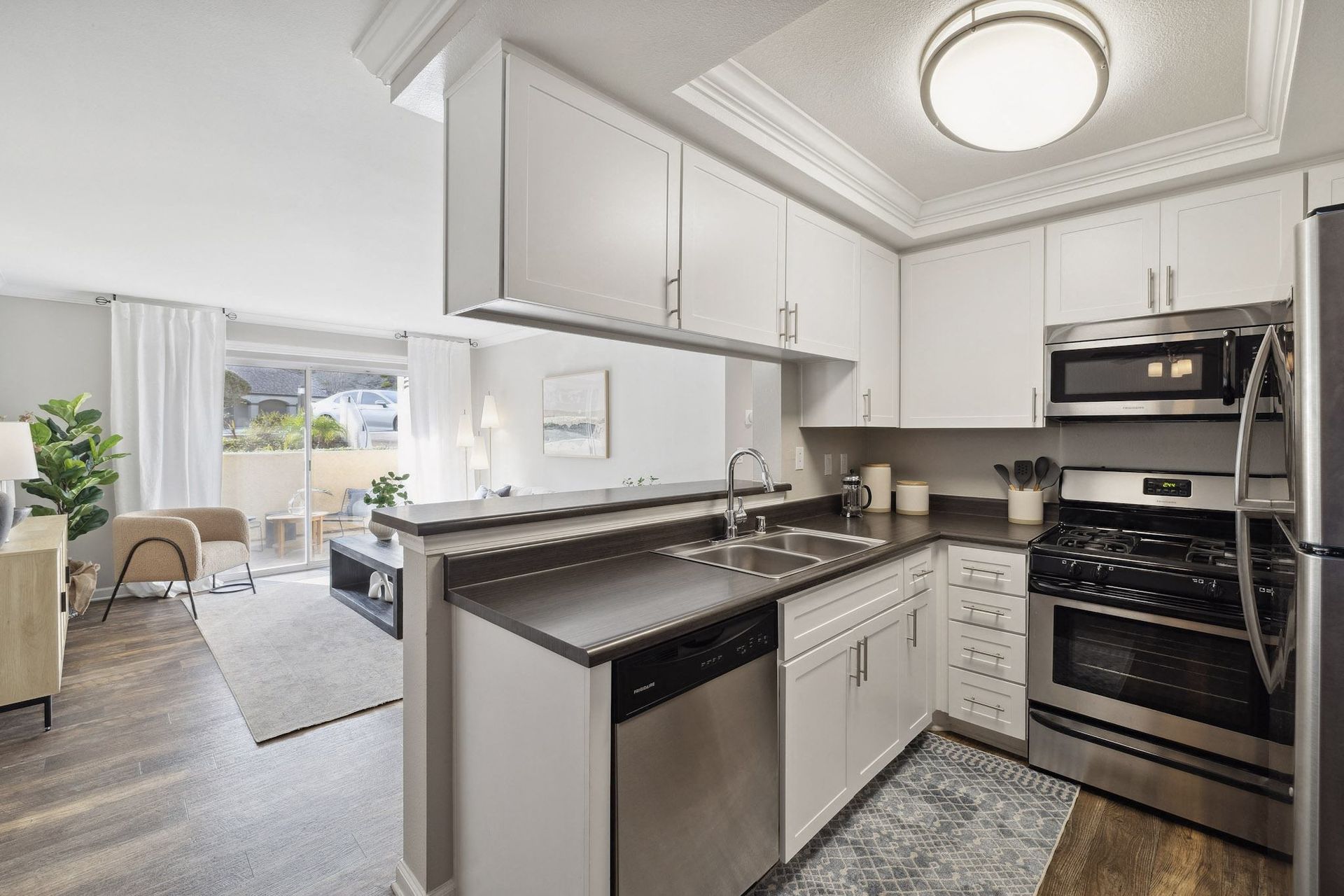 Open-concept kitchen with white cabinets, stainless steel appliances, and a living area beyond.