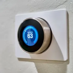 Round smart thermostat on a white wall plate, displaying 63 in blue.