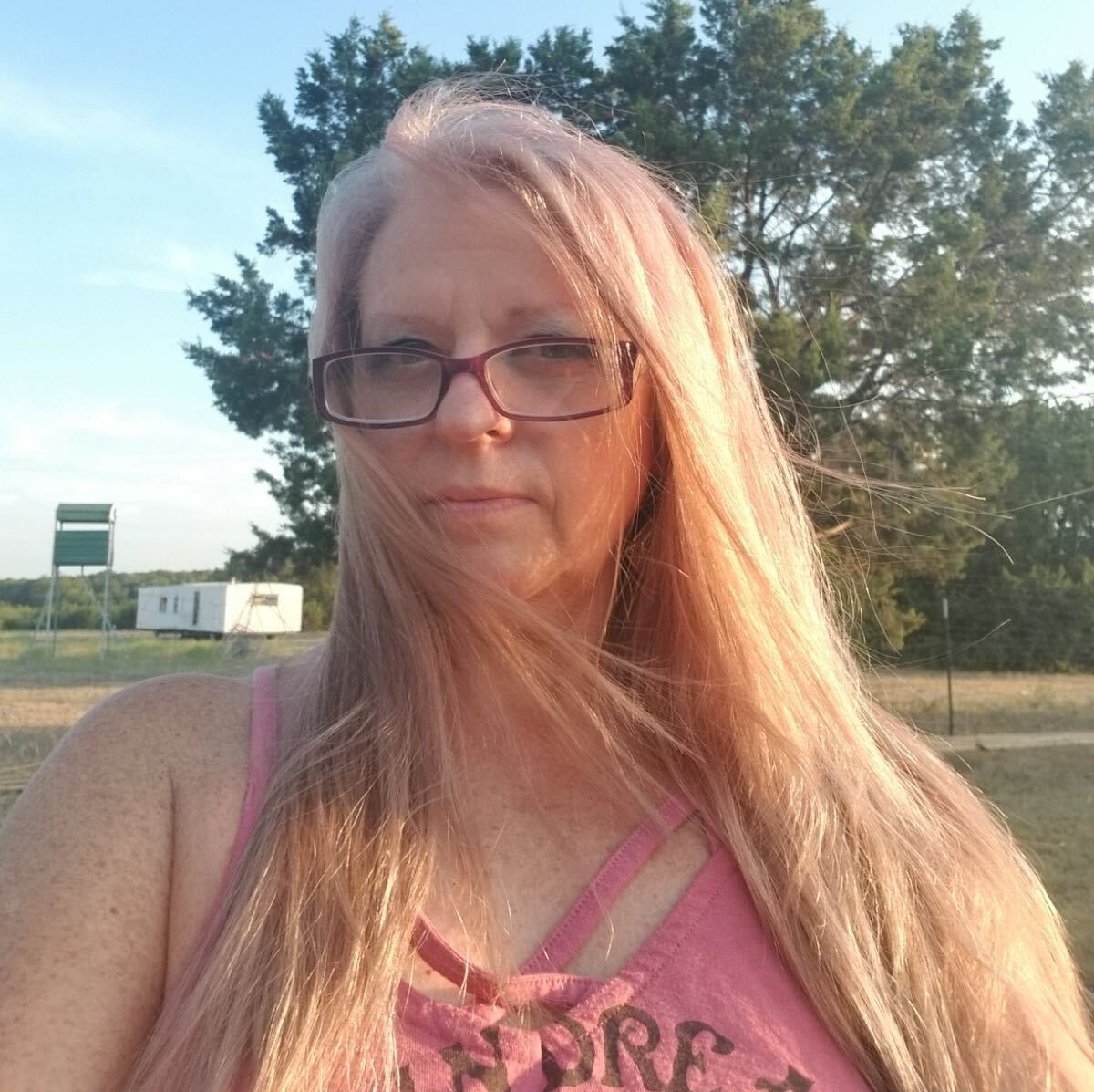 A woman wearing glasses and a pink shirt with the word here on it