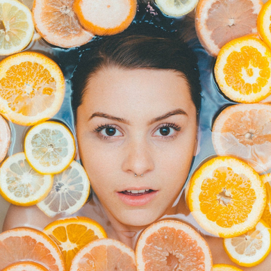 A woman is in a bathtub surrounded by oranges and lemons