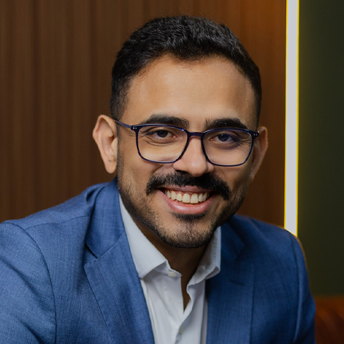 Um homem usando óculos e um terno azul está sorrindo para a câmera.