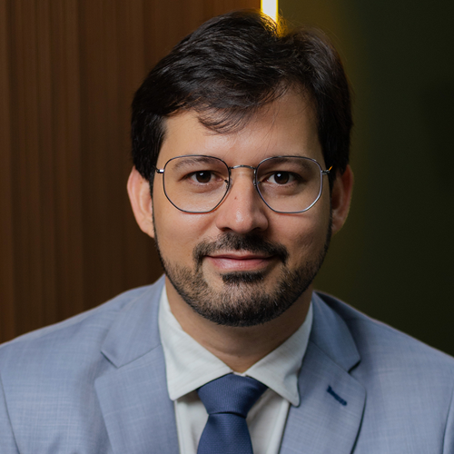 Um homem de terno e gravata usa óculos e barba.