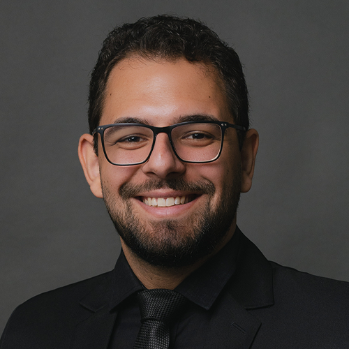 Um homem usando óculos e terno preto e gravata está sorrindo para a câmera.