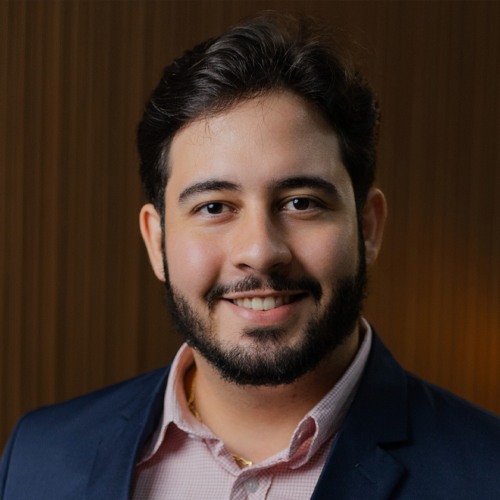 Um homem com barba está vestindo um terno e sorrindo para a câmera.