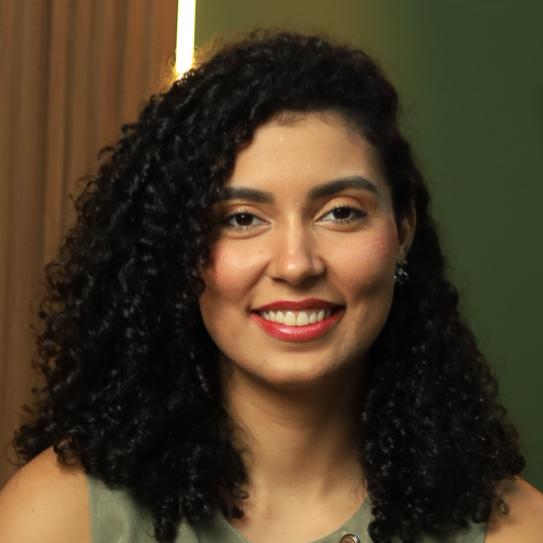 Uma mulher com cabelos cacheados e batom vermelho está sorrindo para a câmera.