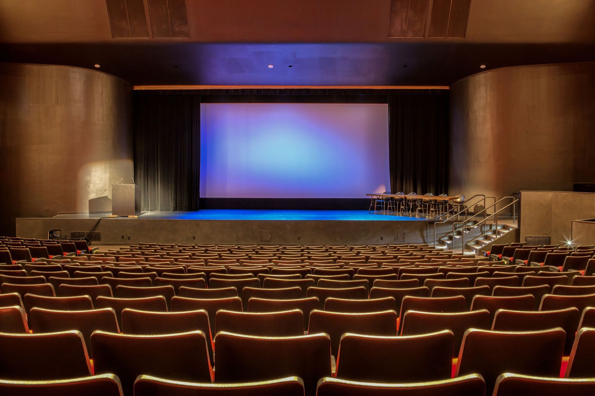 An empty auditorium with rows of seats and a large screen.