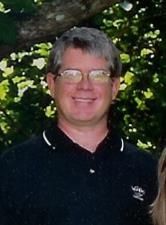 A man wearing glasses and a black shirt is smiling for the camera.