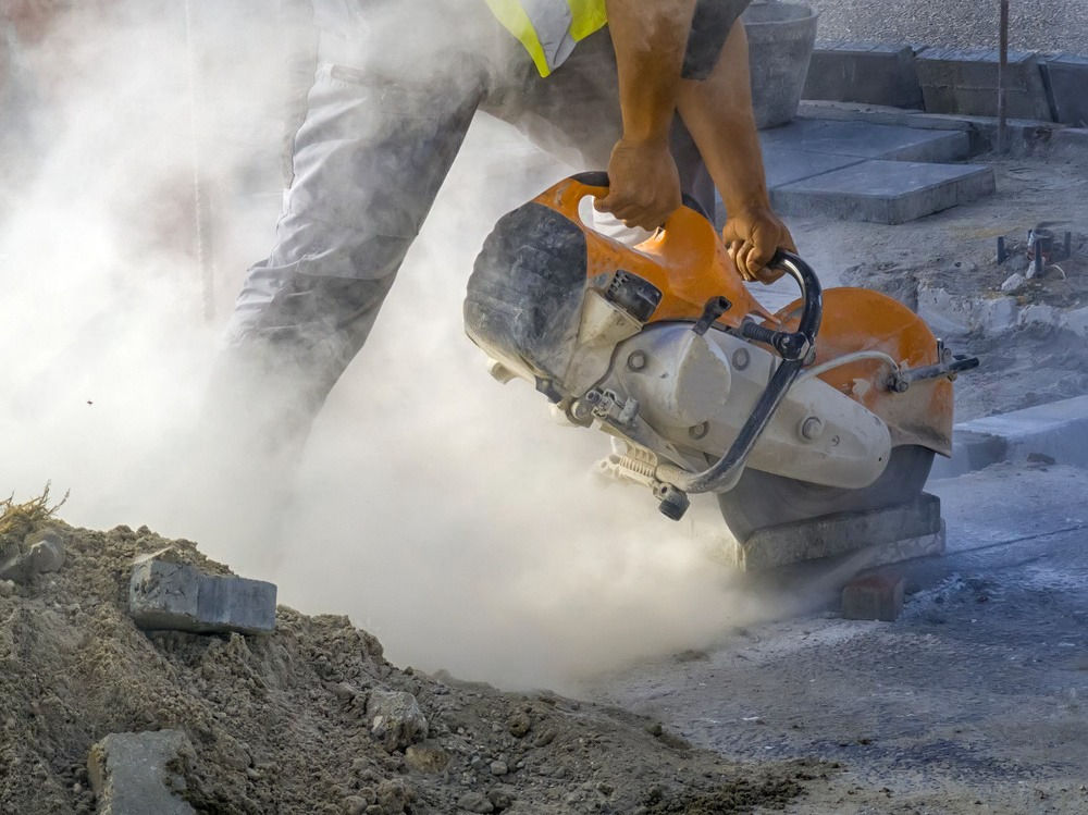 A man is using a concrete saw to cut a hole in the ground.