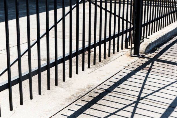 A black metal fence is casting a shadow on the sidewalk - Maywood, IL - Anaya & Sons Fence Company