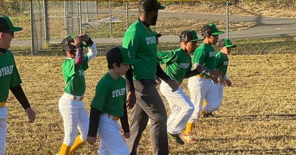 A group of young baseball players are walking on a field with a coach.