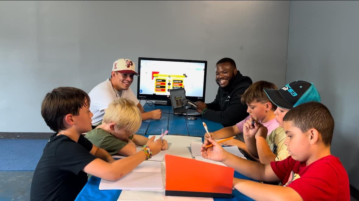A group of young boys are sitting around a table in front of a computer.