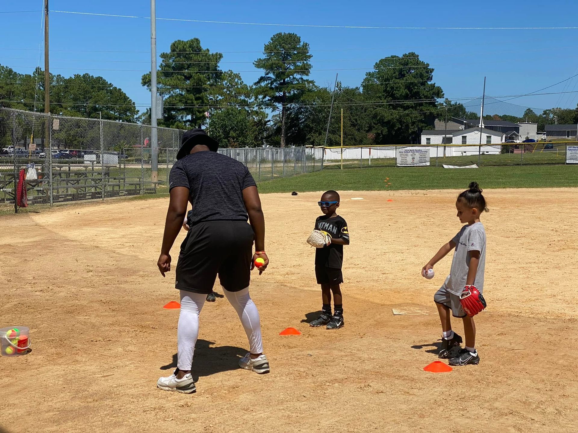 A man and two children are playing baseball on a dirt field.
