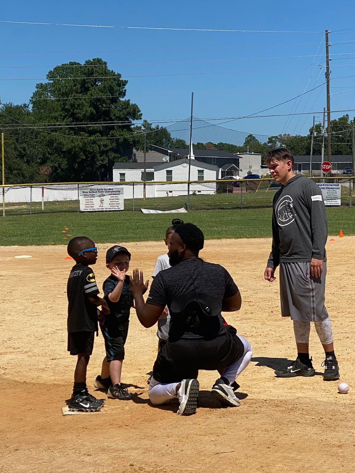 A group of young boys are standing on a baseball field with a man kneeling down.