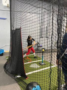 A young girl is swinging a bat at a ball in a batting cage.