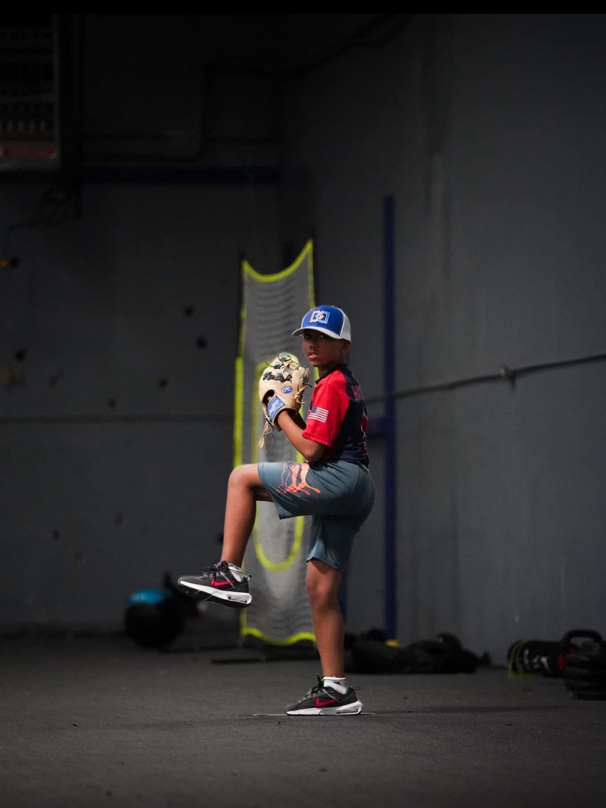 A young boy is pitching a baseball in a dark room.