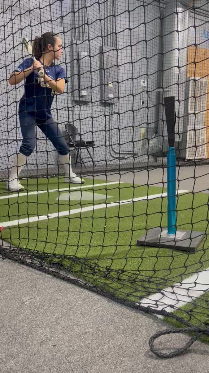A woman is swinging a bat at a ball in a batting cage.