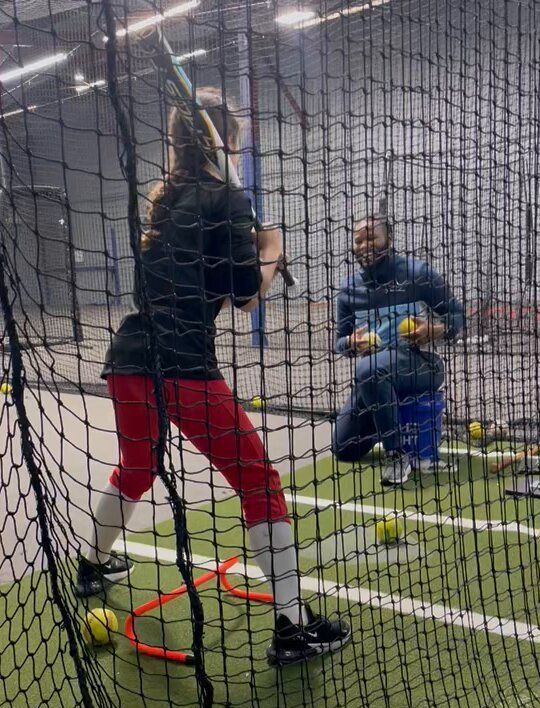 A woman is swinging a bat at a baseball in a batting cage.