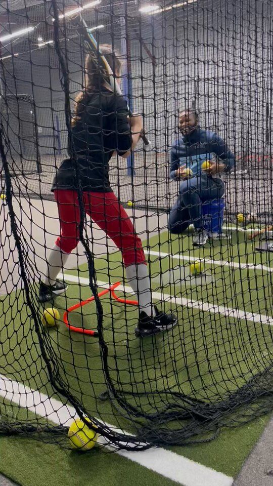 A woman is swinging a bat at a baseball in a batting cage.