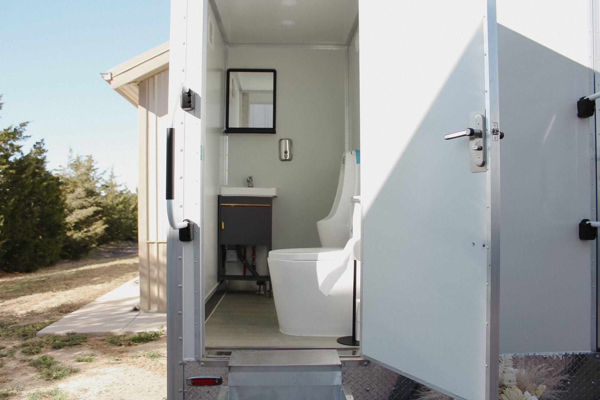Four teal portable toilets in a row against a wall on a concrete pad.