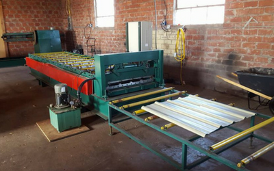 Industrial machine feeding white metal sheets in a workshop with brick walls and windows