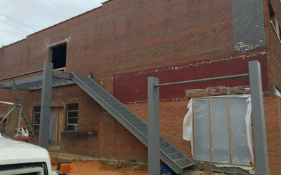 Metal stairs and railing attached to a red brick building under construction, with a covered structure beside it