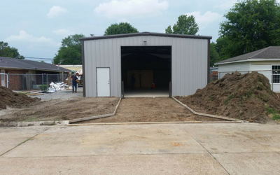 New metal garage with open door at a construction site, dirt piles on both sides