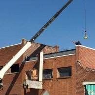 Crane lifts material above red brick building with a worker hanging from the hook