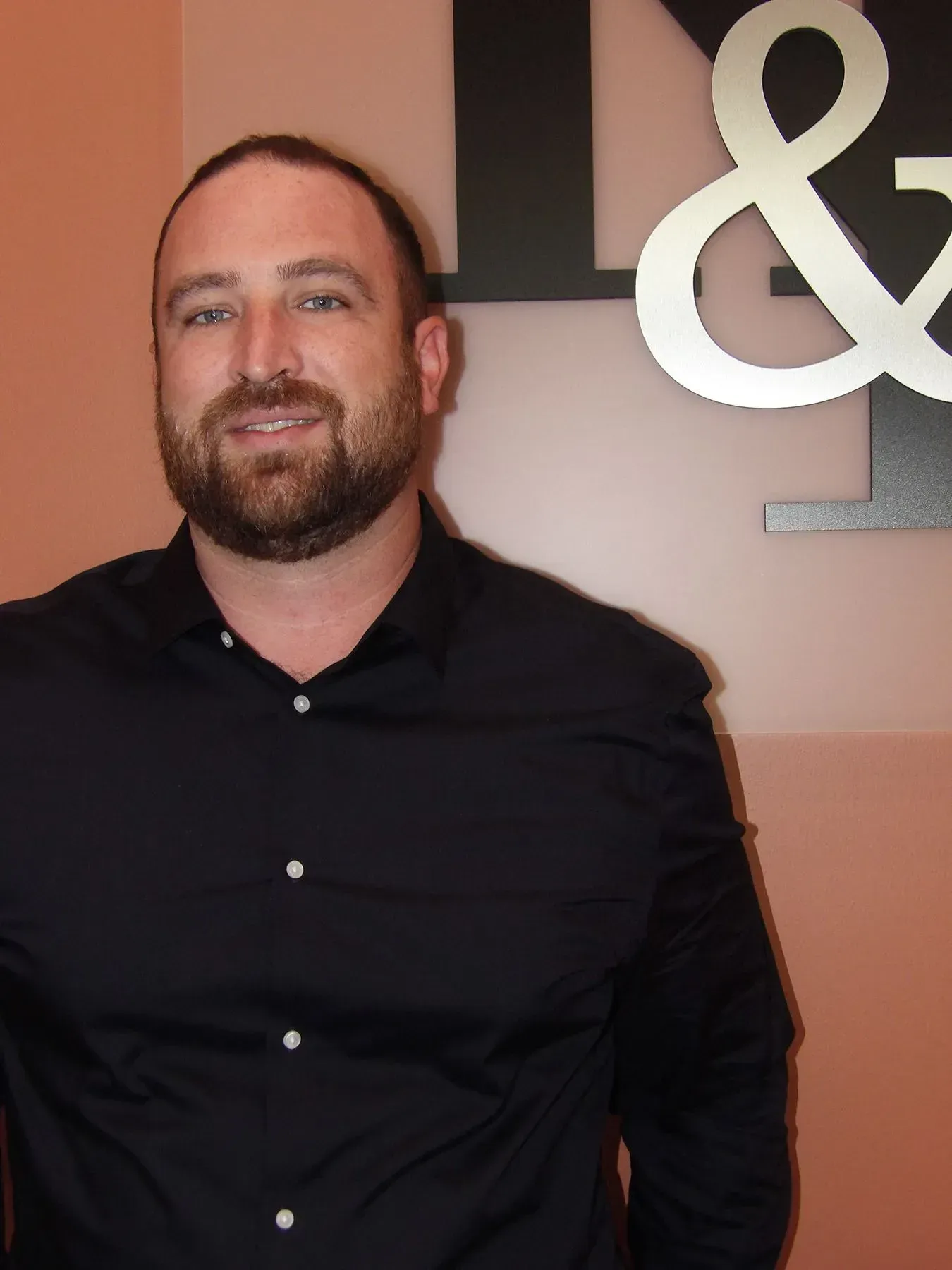 Man with beard, wearing black shirt, standing next to a large