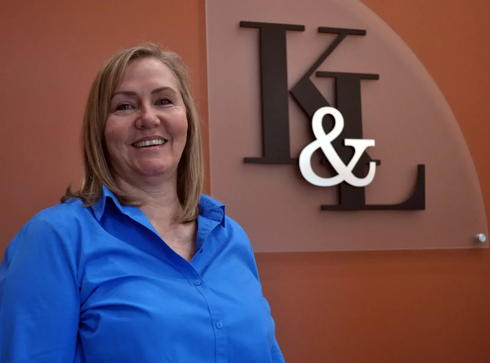 Woman in blue shirt smiling, standing near a sign with the letters