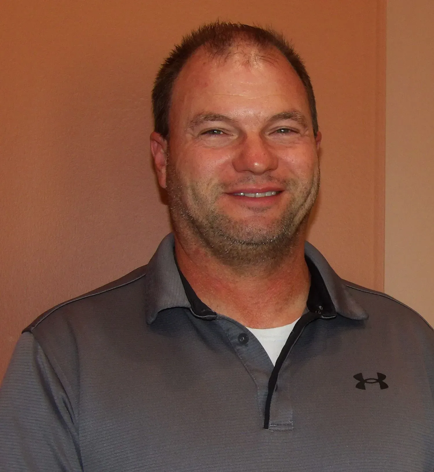 Smiling man in gray Under Armour polo shirt, looking at the camera.