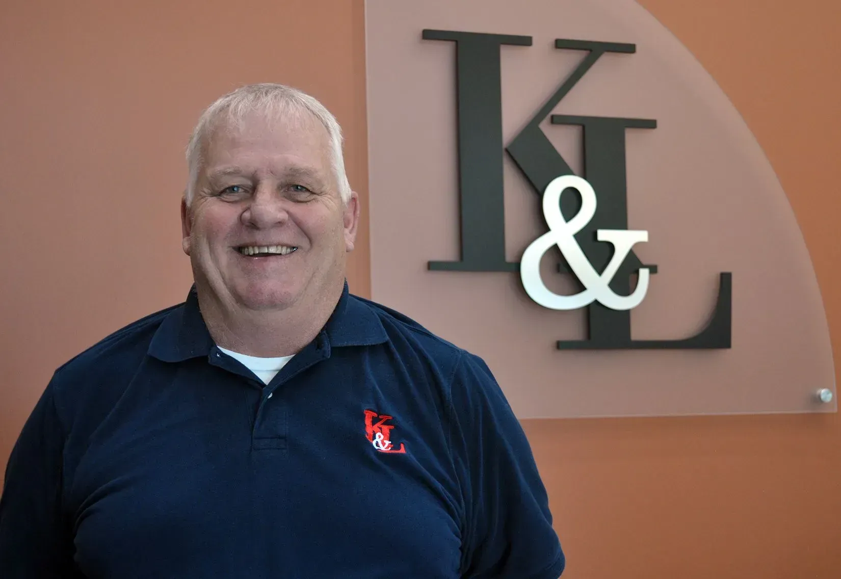 Man in blue shirt smiles in front of a sign with