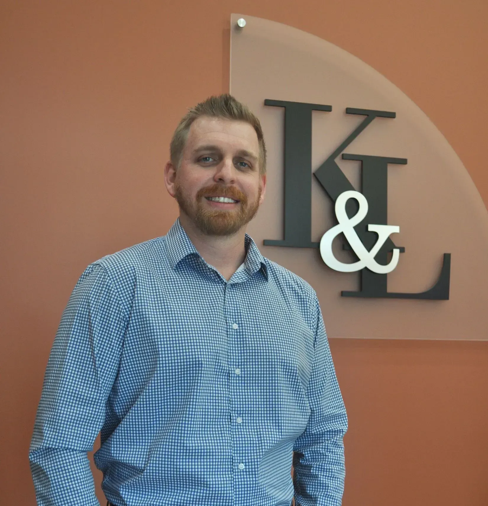 Man with a beard smiling, stands in front of a sign with