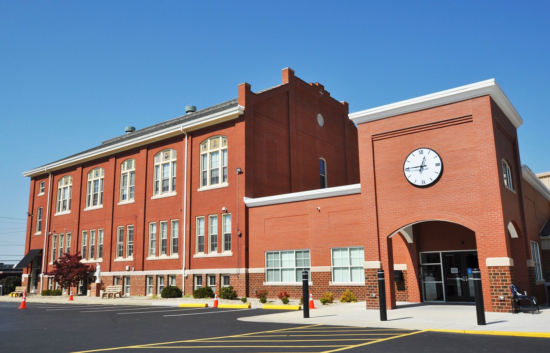 Red brick school building with clock tower and entrance under a blue sky.