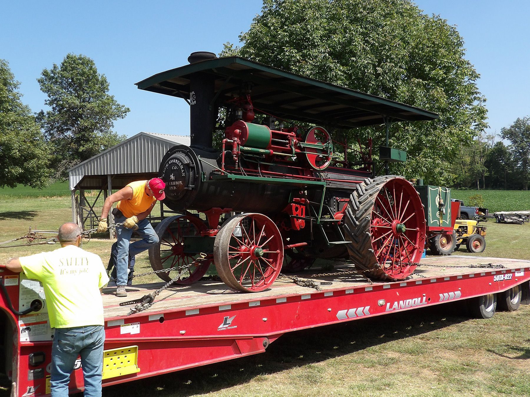 Man reading book to unseen audience in a library, pointing at a construction vehicle image.