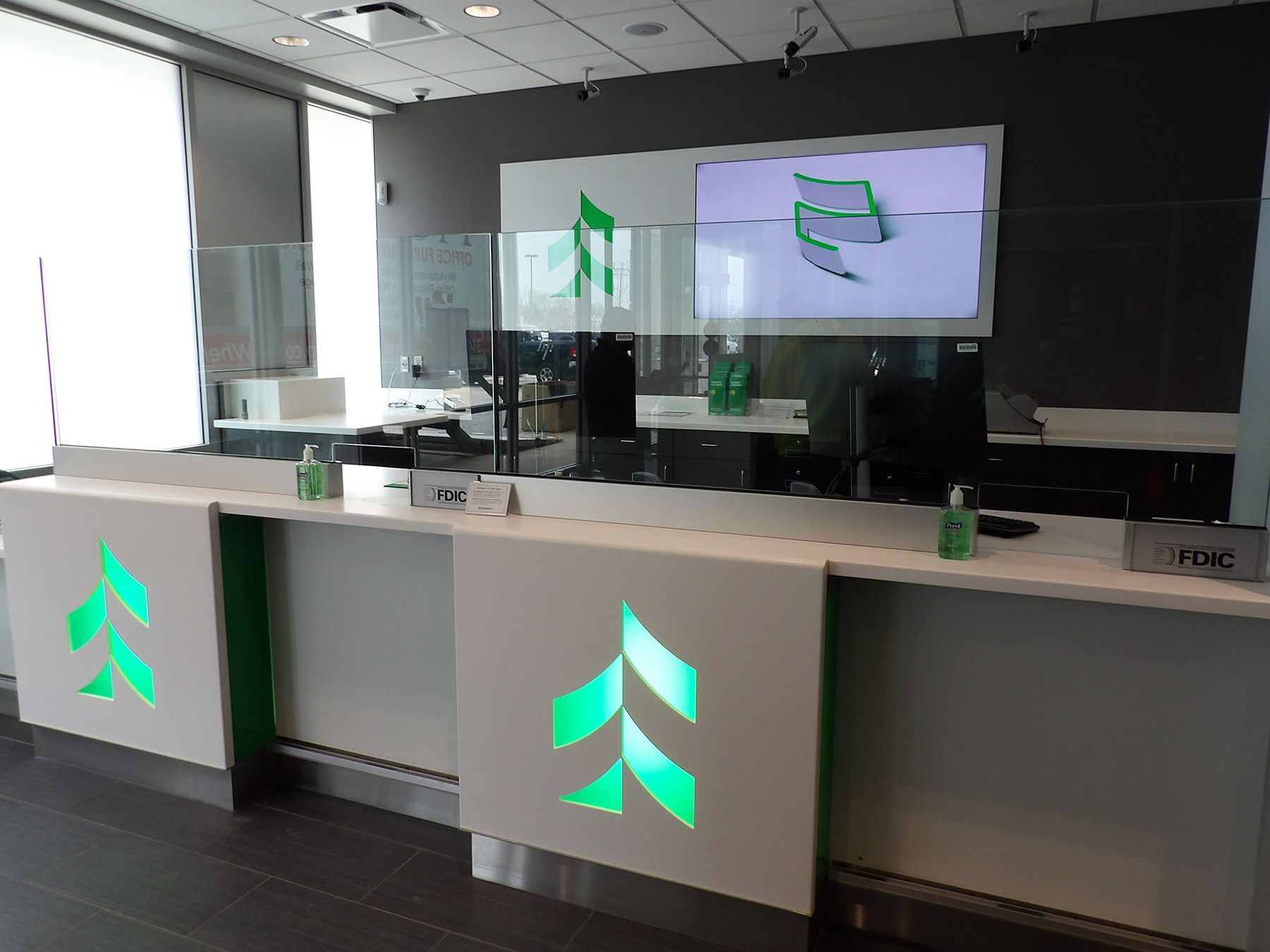 Bank teller counter with green logo and protective dividers.