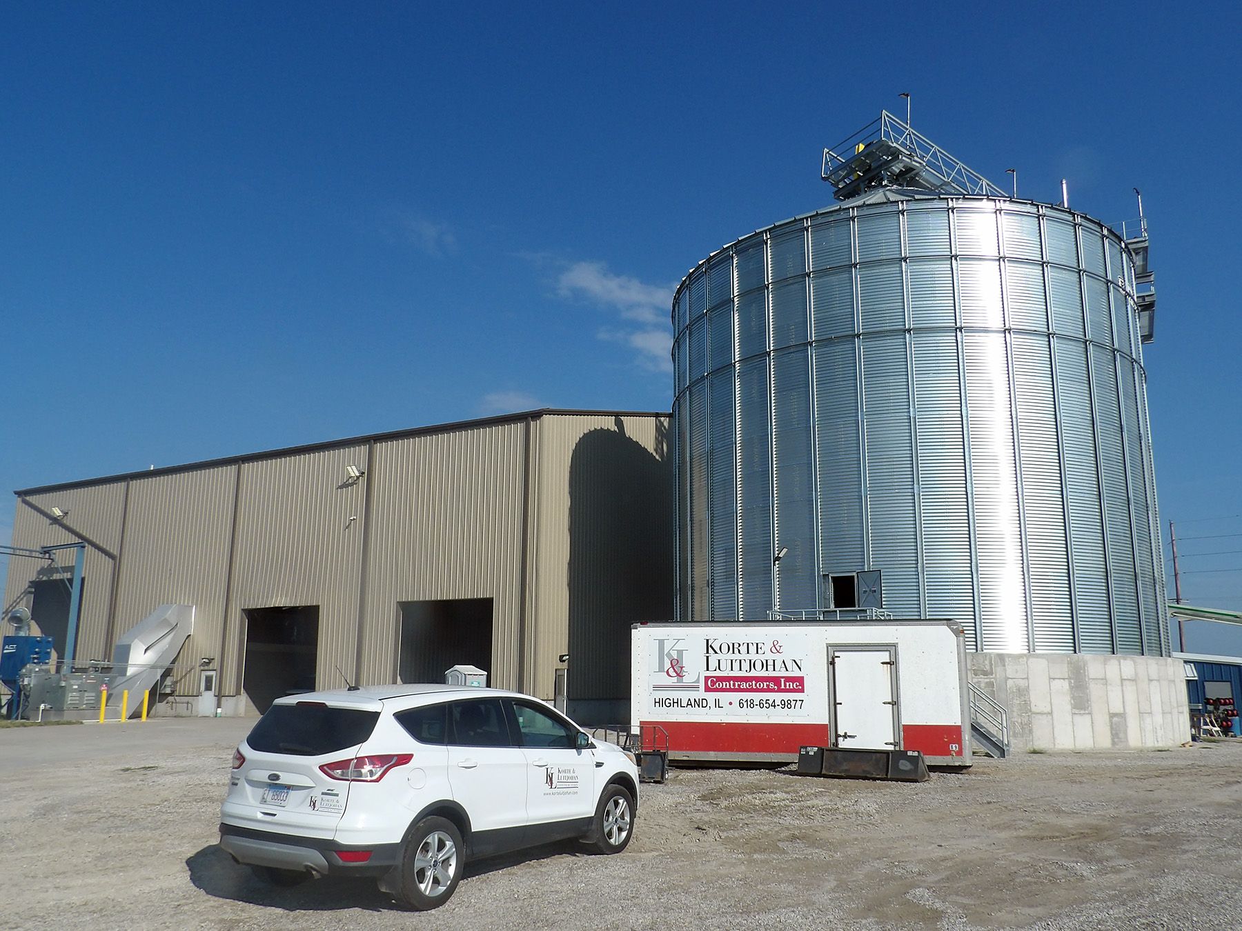 White SUV parked near a grain silo and industrial building on a sunny day.