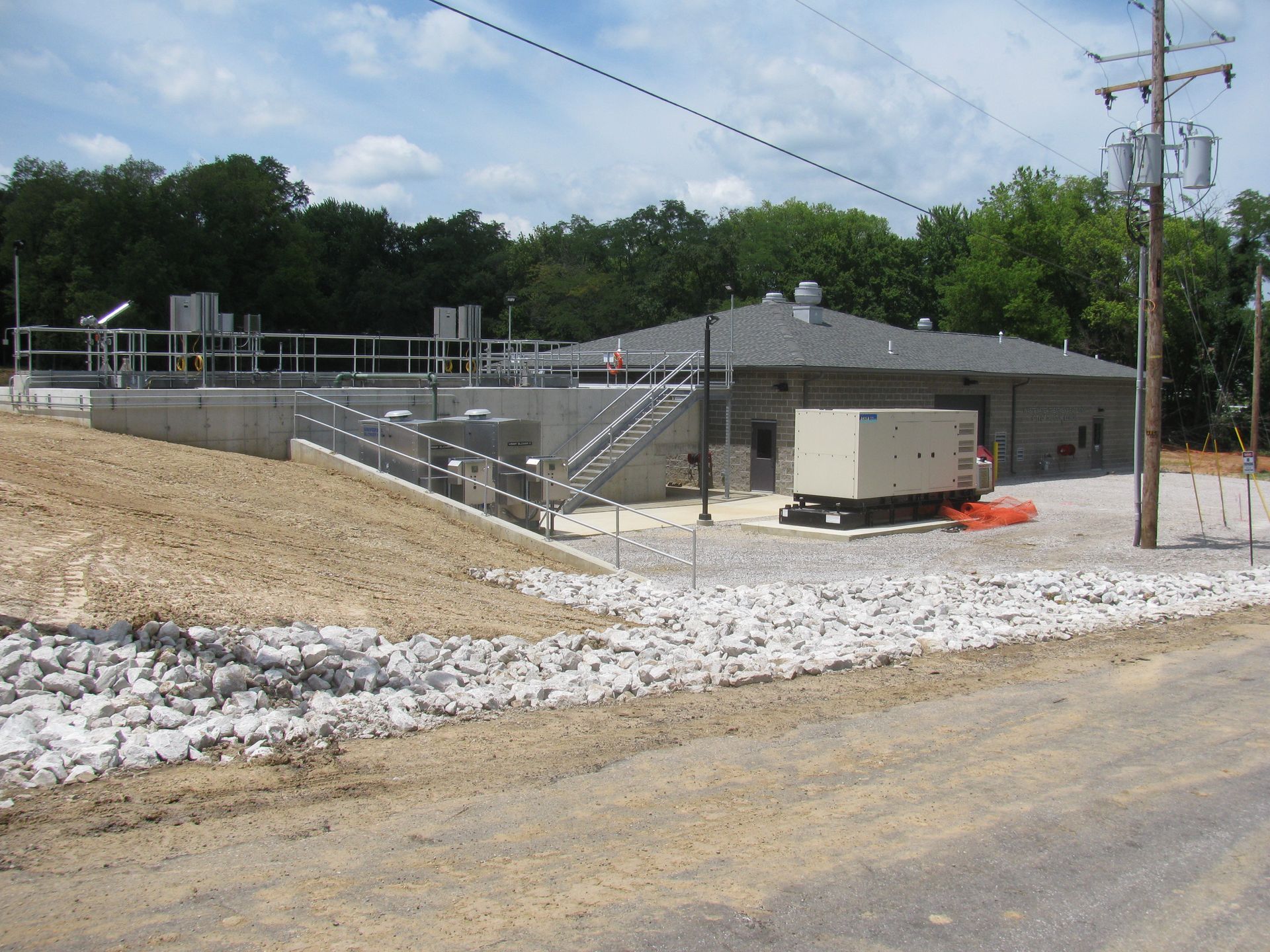 Exterior view of a water treatment facility with a building, machinery, and a gravel lot.