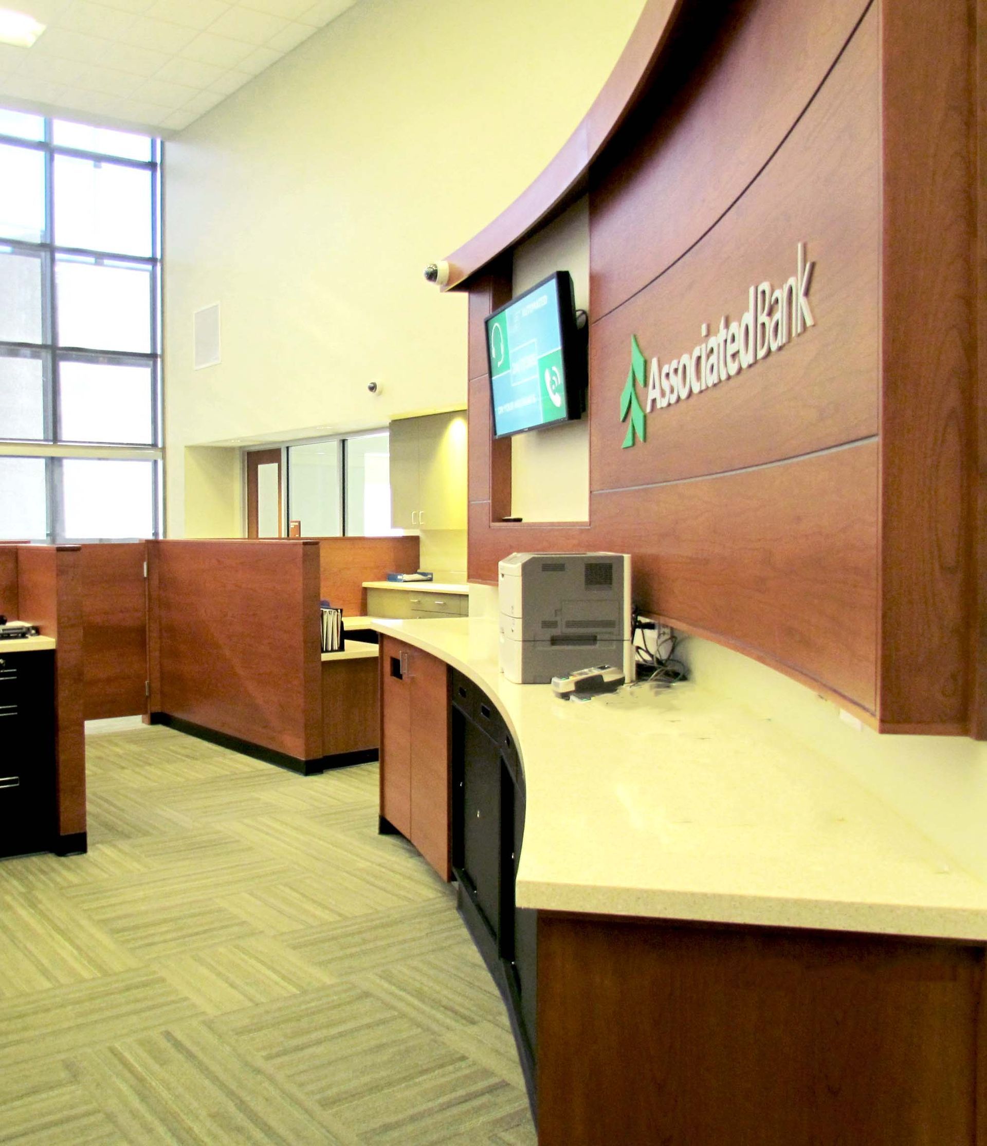 Interior of an Associated Bank, featuring curved wooden counter, check-in stations, and large windows.