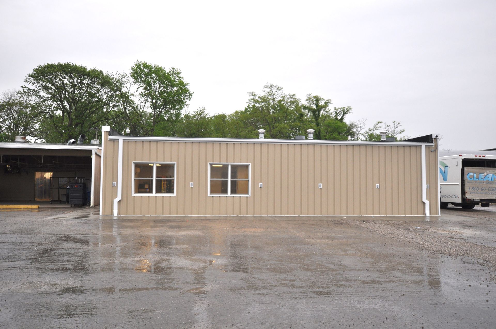 Tan building with two windows and a flat roof in a rainy parking lot.
