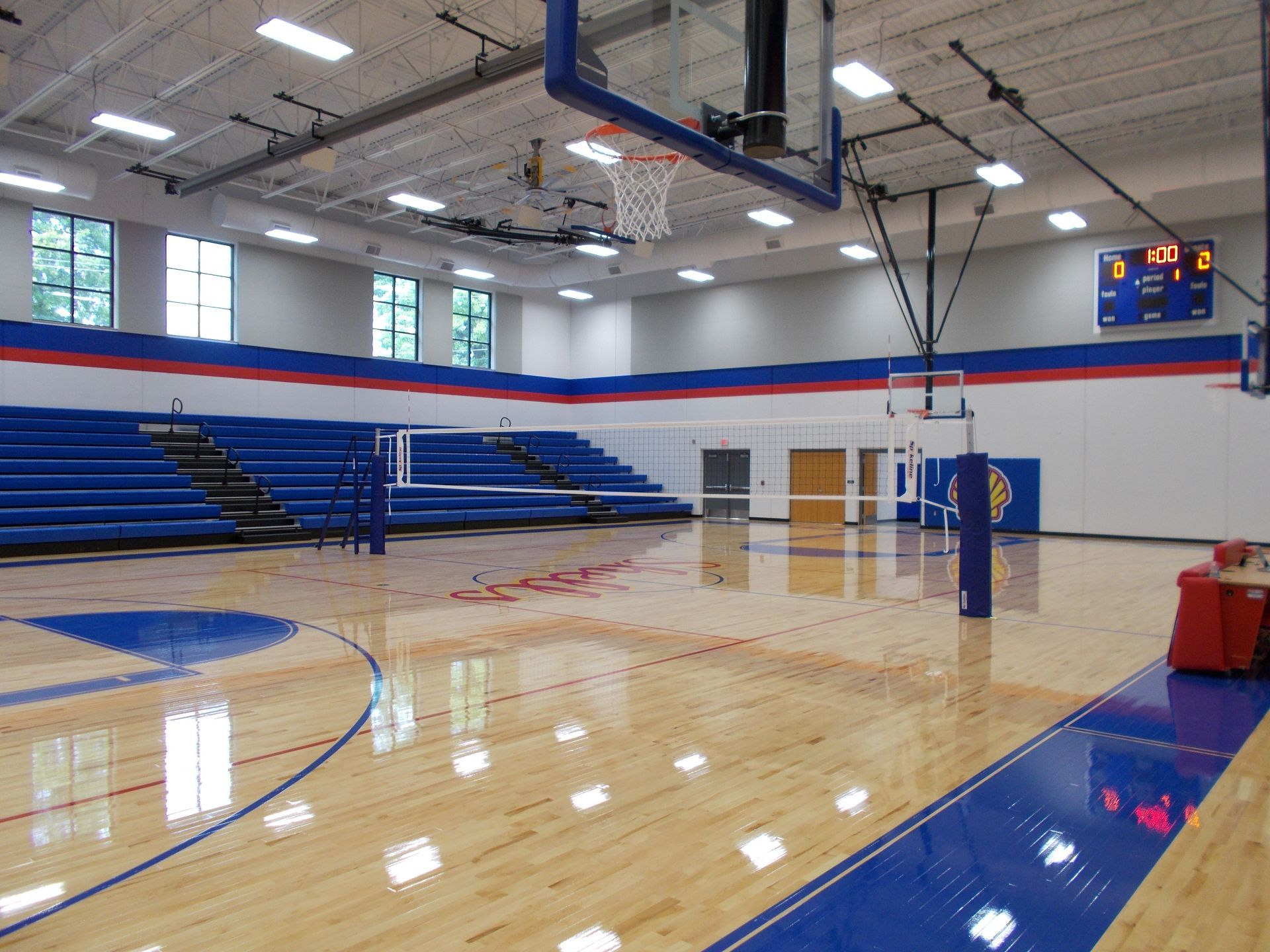 Basketball court with blue and red accents, bleachers, and a scoreboard.